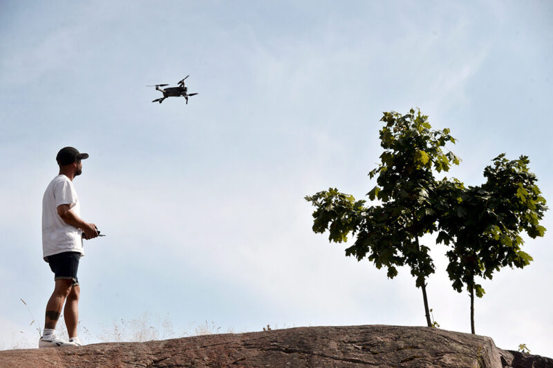 Kesäisesti pukeutunut mies seisoo kalliolla ja lennättää dronea.