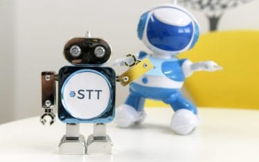 Kaksi lelurobottia, joista toiseen on liimattu STT:n logo, seisoo pöydällä.