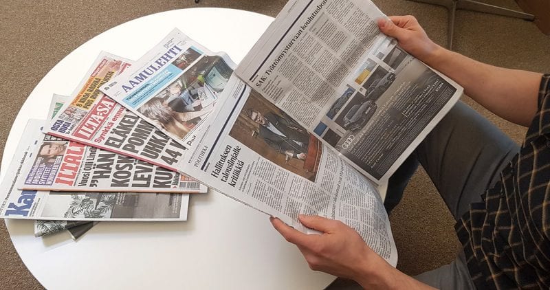 Mies lukee Helsingin Sanomia sanomalehtipino pöydällä vieressään.