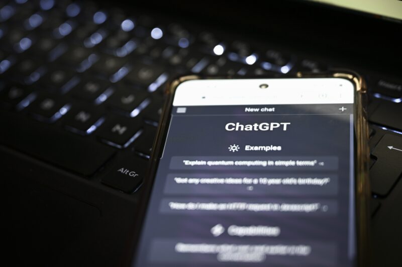 Tietokoneen näppäimistön päälle on asetettu matkapuhelin, jolla käytetään ChatGPT-tekoälysovellusta.